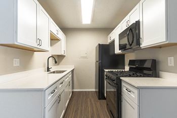 An empty kitchen with white cabinets and a black stove and microwave